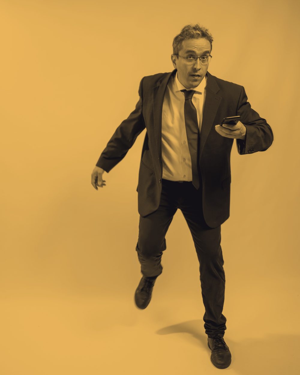 Felice Marra in giacca e cravatta, smartphone in mano, in un'elaborazione bicromatica ambra.
