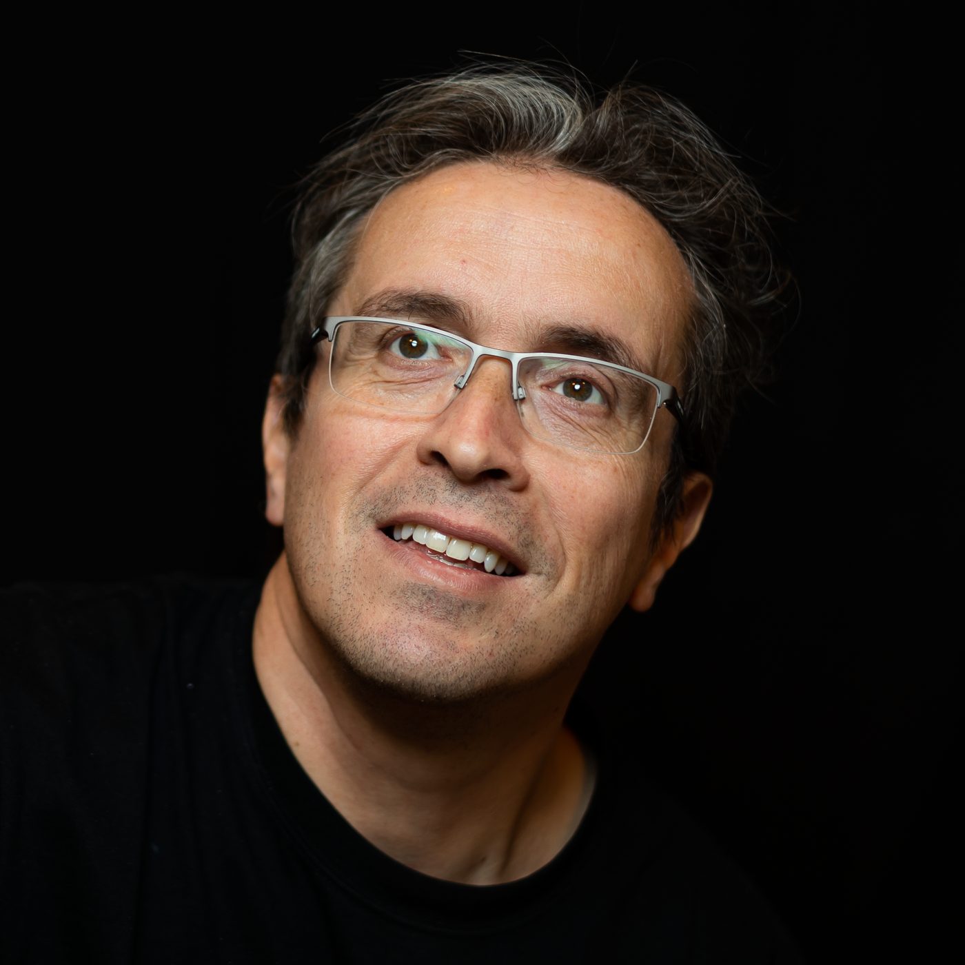 Ritratto di Felice Marra su fondo nero, sorridente, con occhiali.